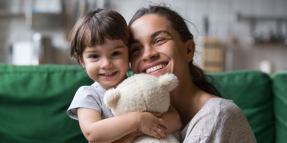 Mom and daughter hugging, smiling, and looking camera
