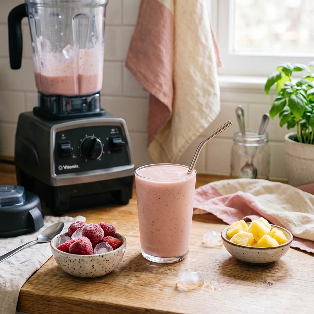 Batido de fresa y piña sobre la encimera, junto a una batidora