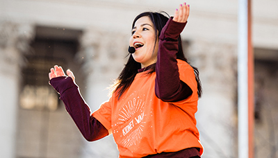 a woman wearing a microphone dancing a clapping on stage at a National Kidney Foundation event