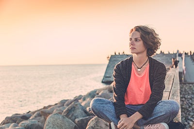 a woman sitting on a sea wall looking at the ocean