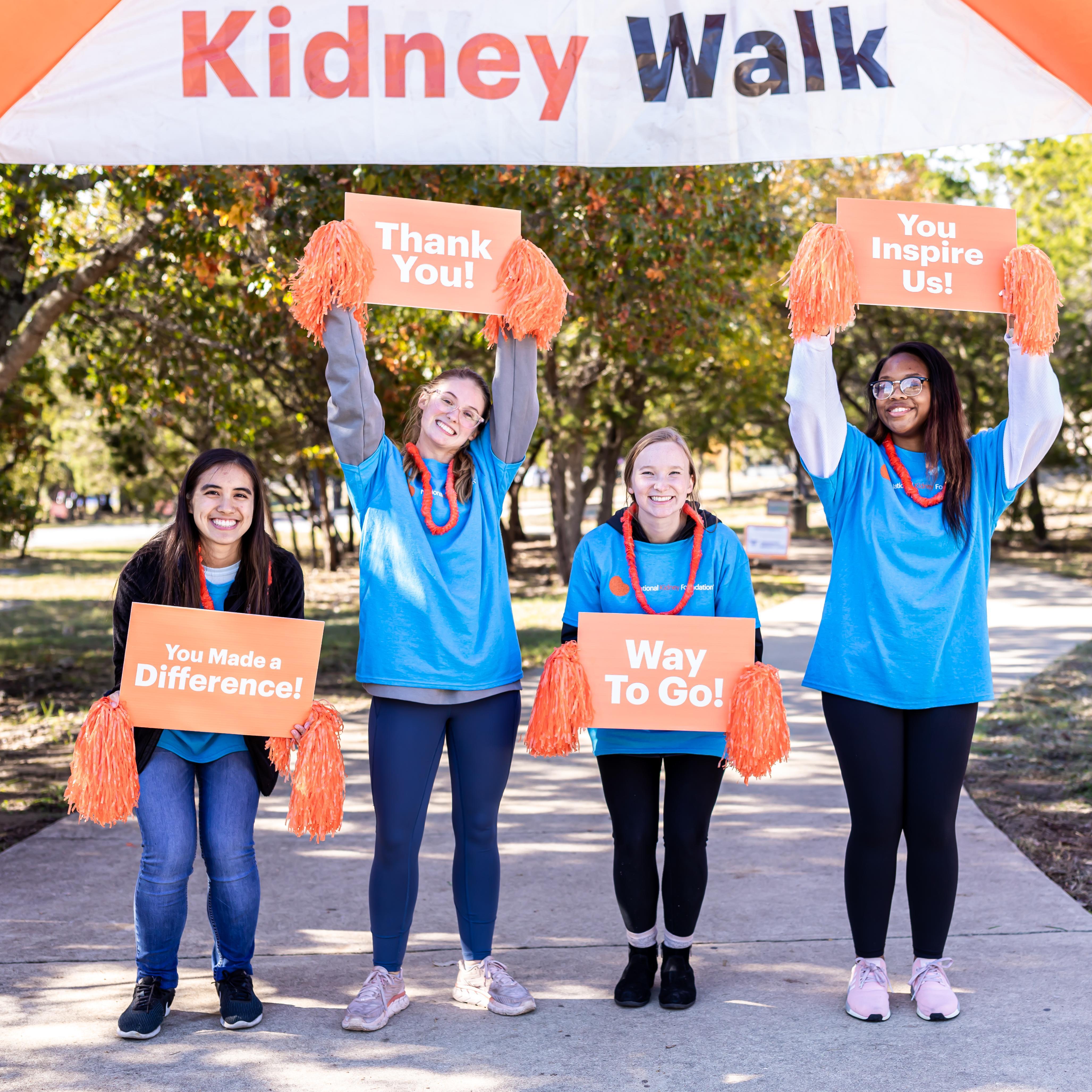 Four individuals holding signs of encouragement under a Kidney Walk Arch