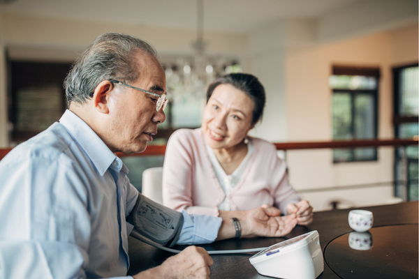 Person measuring blood pressure with partner at kitchen table