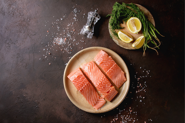 Uncooked salmon on a plate next to cut lemon and salt