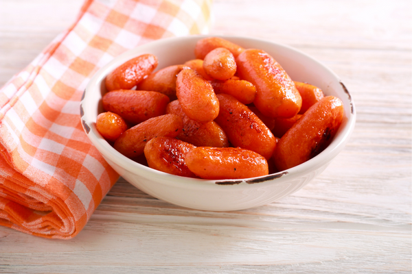 Glazed carrots in bowl next to cloth napkin