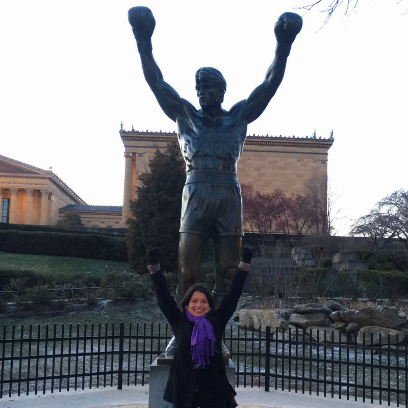 Isha with arms up in front of Rocky statue
