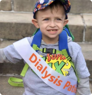 Jax, a small child, wears a "Dialysis Patient" sash