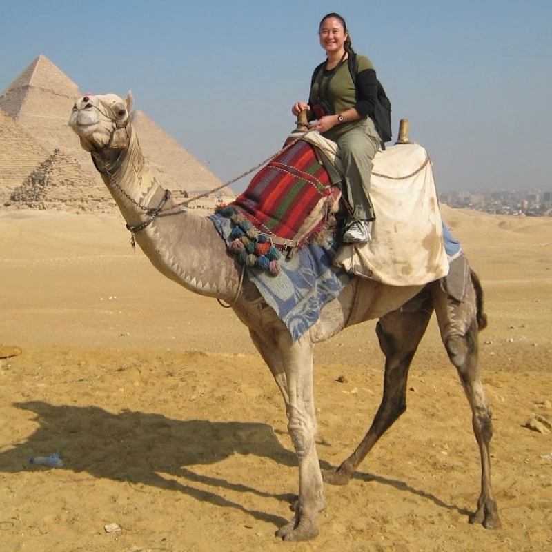 June smiling on a camel with pyramids behind her