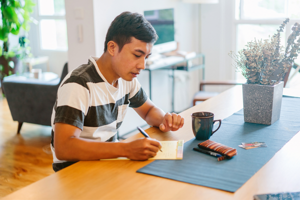 person writing in notebook at dining room table