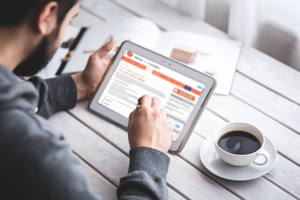 man using ipad while sitting at a table with coffee