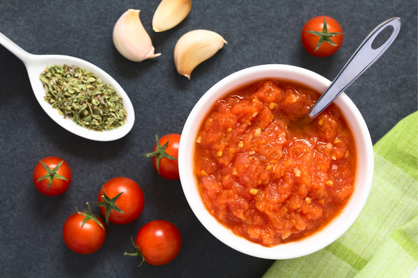 Crushed tomatoes in a bowl with whole tomatoes and garlic nearby