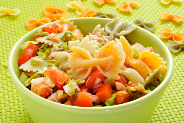 Bowl of pasta salad with raw bow tie shells in the background