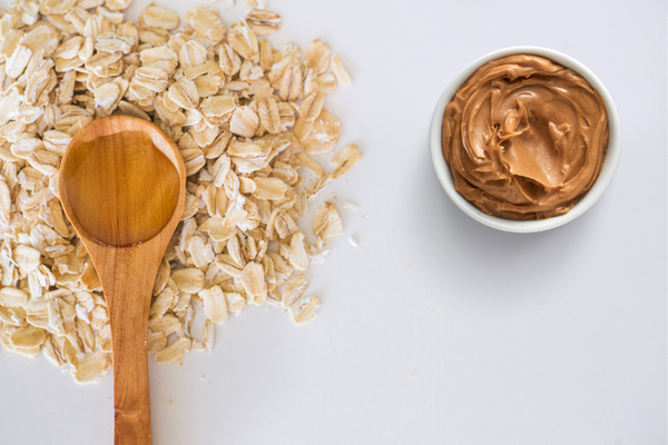 Wooden spoon on pile of oats with small bowl of peanut butter nearby