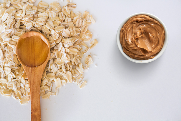 Cuchara de madera sobre un montón de avena con un pequeño tazón de mantequilla de maní cerca