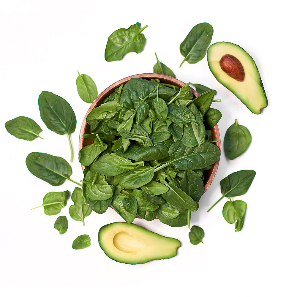 Spinach in a wooded bowl with avocado on the side