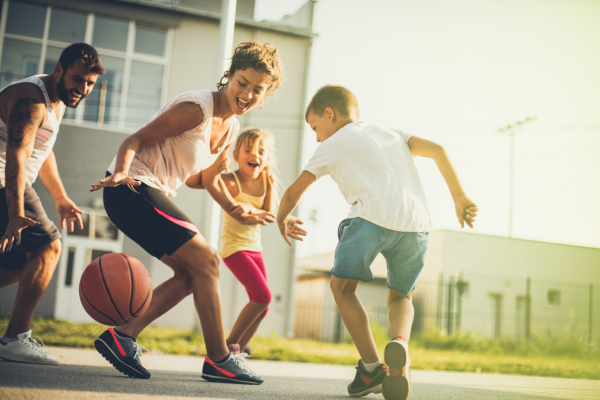 Happy adults playing basketball with smiling children
