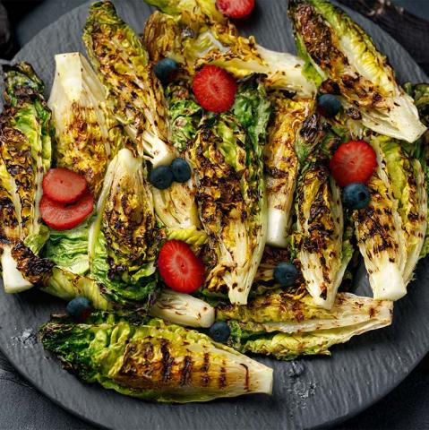 grilled romaine wedges on a plate with strawberry slices and whole blueberries