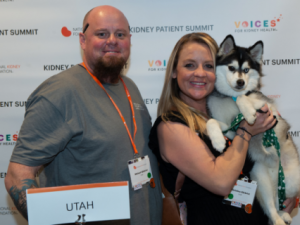 Christina, Michael, and seeing-eye dog Moose in front of Voices for Kidney Health Banner