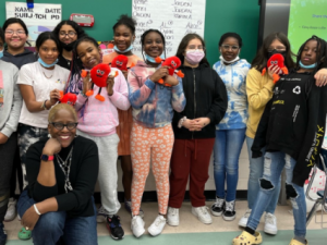 Girls Inc. group smiling in a classroom holding stuffed cartoon kidney.