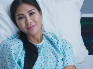 Persona sonriente recostada en una cama con bata de hospital.