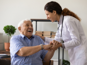 Older person smiling and holding healthcare professional's hand. 