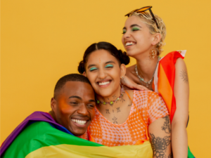 Three people holding each other with LGBTQIA+ flag