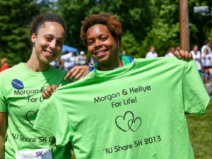 Kellye Miller smiling behind Morgan Reid holding a shirt that says "Kellye and Morgan for Life"