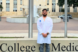 Andrew in front of medicine school in doctor coat