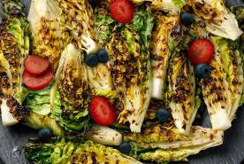 grilled romaine wedges on a plate with strawberry slices and whole blueberries