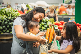 Small child holding carrots up to baby being held