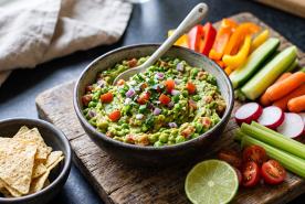 Guacamole with toppings and raw veggies on the side