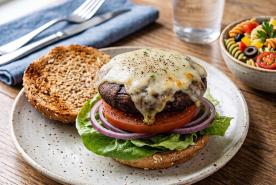 Portobello mushroom burger topped with swiss cheese, on a whole wheat bun, with tomato, lettuce and red onion.