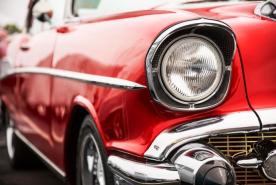 Primer plano del faro delantero y los detalles cromados de un coche clásico de color rojo brillante.