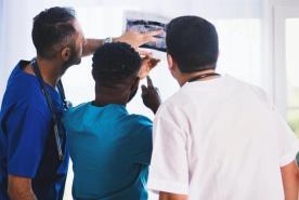 Tres profesionales sanitarios examinan juntos una radiografía, señalando la imagen en un luminoso entorno clínico.