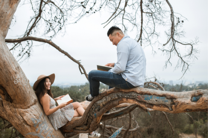 Dos personas contentas leyendo libros bajo un gran árbol