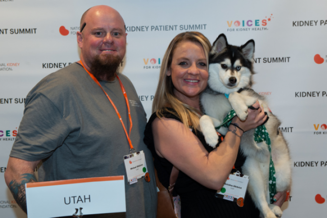 Christina, Michael, and seeing-eye dog Moose in front of Voices for Kidney Health Banner