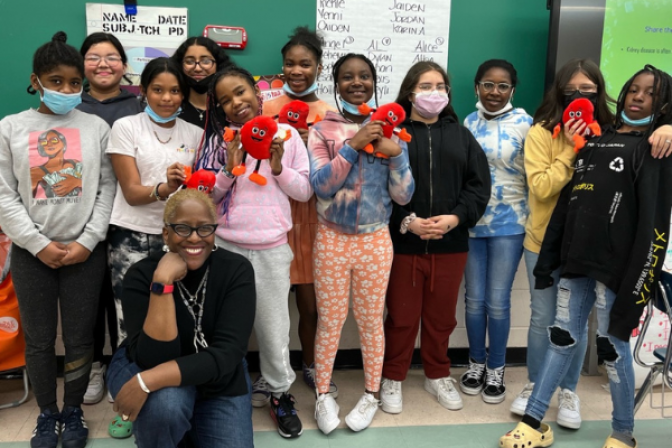 Girls Inc. group smiling in a classroom holding stuffed cartoon kidney.