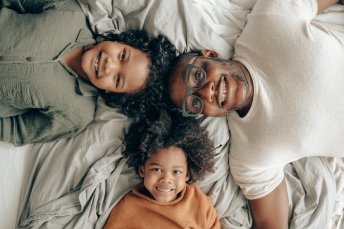 Parent with two children laying on bed smiling 