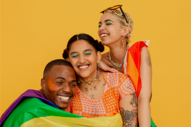 Three people holding each other with LGBTQIA+ flag