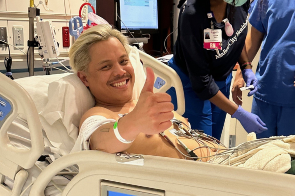 Larry giving thumbs up in hospital hooked up to many machines.