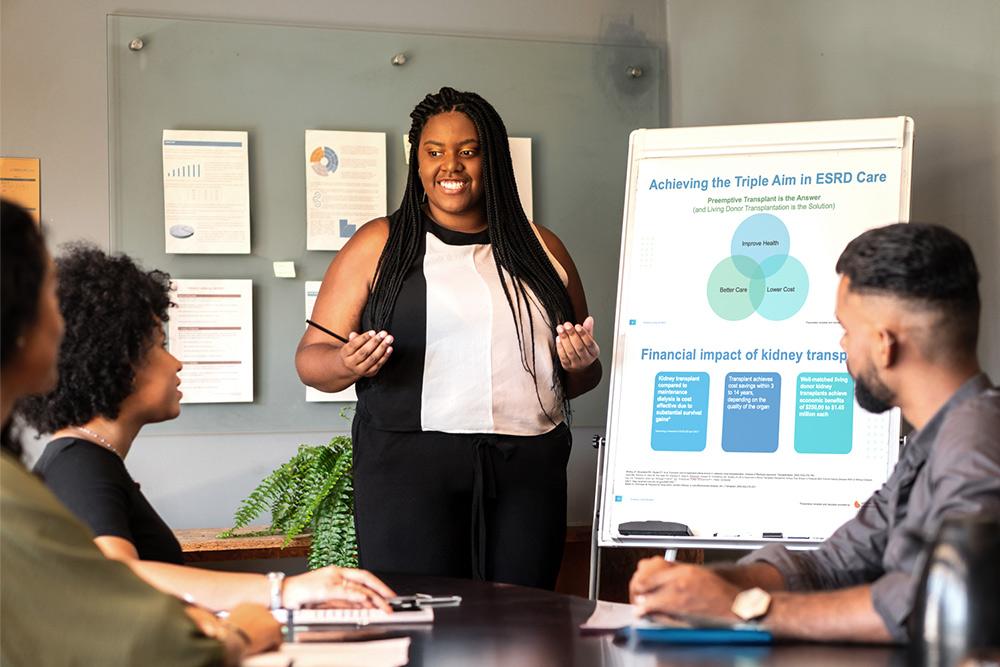 Woman presenting a Living Donation Business Case to a group of people in a conference room