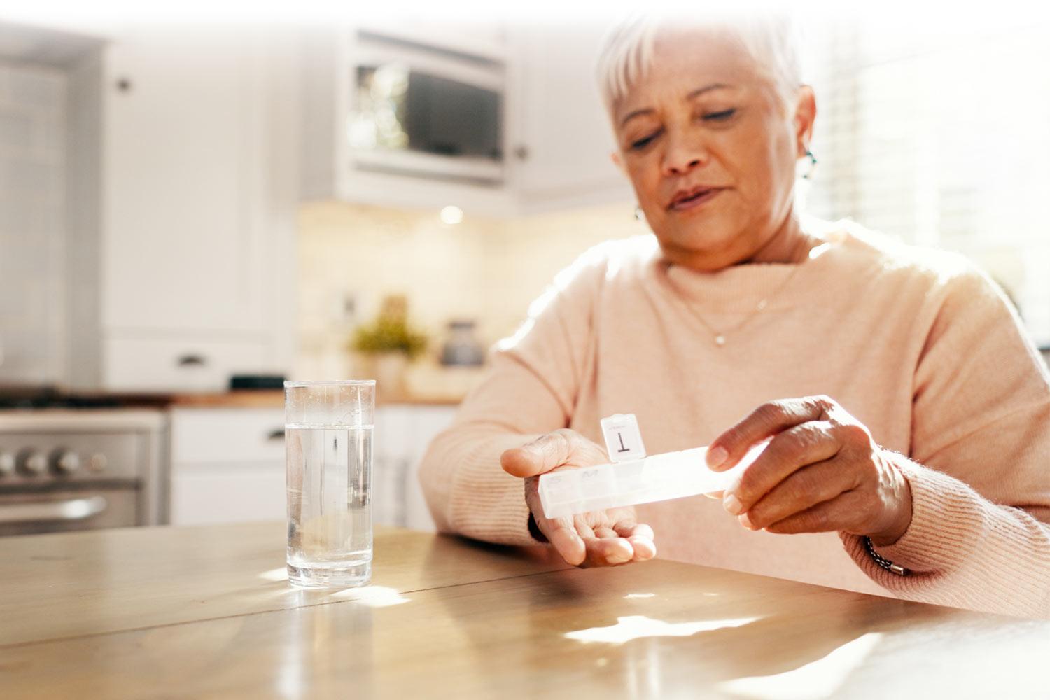 Woman taking her medicine from a pill box at a kitchen table