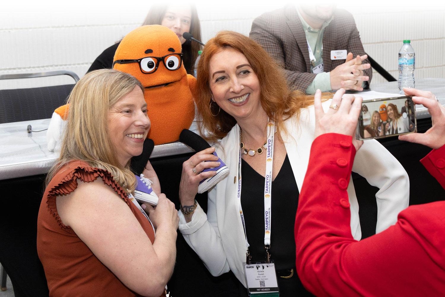 Two attendees getting a selfie with Kenny the Kidney, NKF's mascot