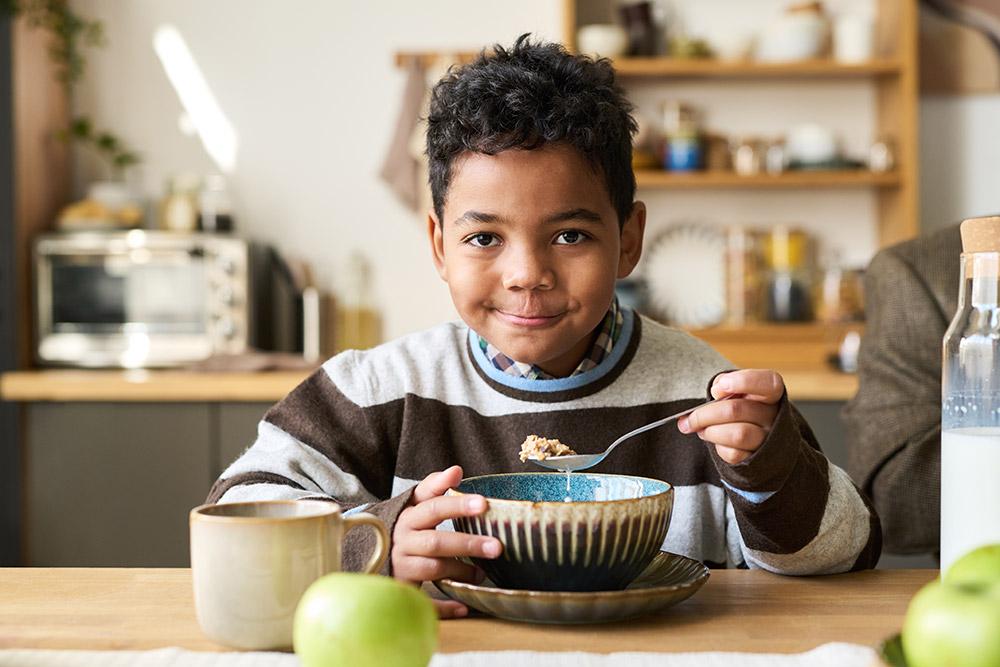 Happy boy eating breakfast cereal at kitchen table