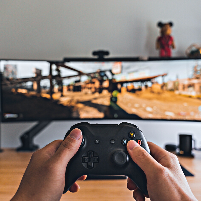 Hand holding a video game controller in front of computer monitor