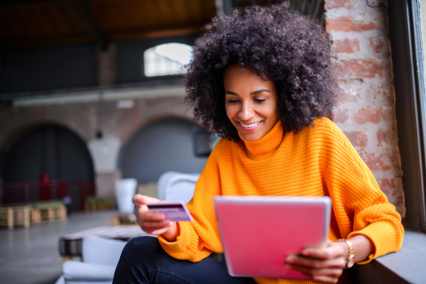 Person smiling while holding a credit card and looking at tablet