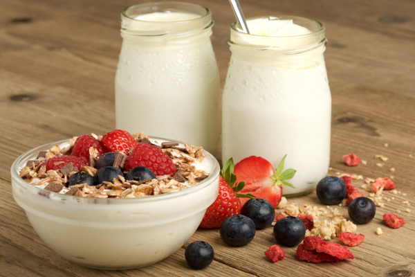 Bowl of yogurt covered fruit with two plain yogurt bottles.